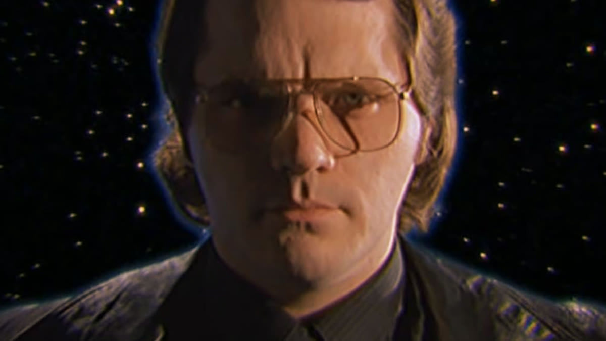 Garth Marenghi wearing glasses and a black leather jacket standing in front of a background of stars.
